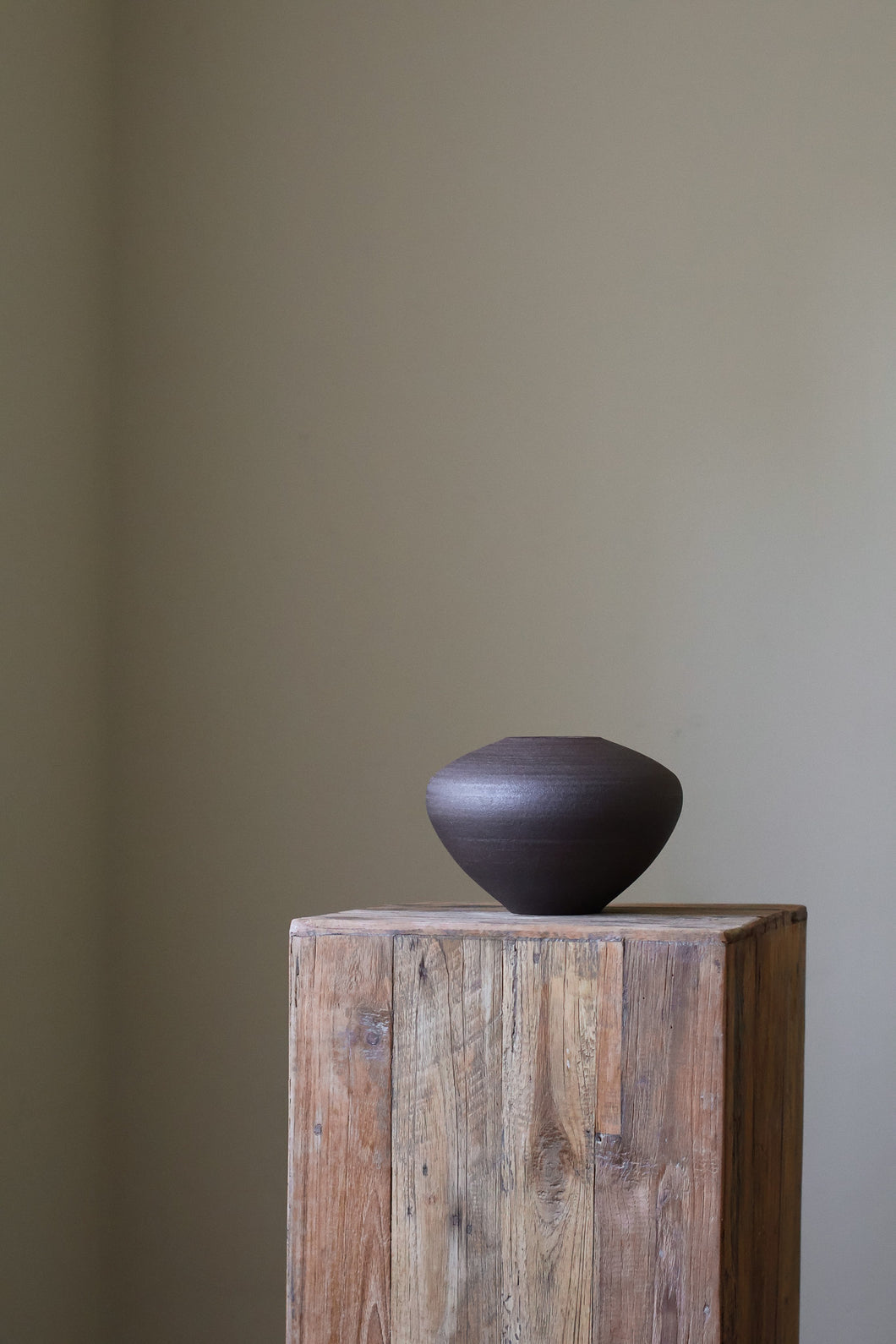 Contemporary sculptural bowl in a dark, earthy tone, featuring a richly textured surface and a simple, rounded form