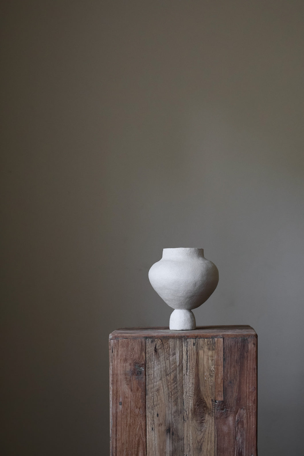 A hand-built, matte white sculptural vase by Hana. The vase features a generously rounded, almost bulbous body that tapers dramatically to a slender, short neck. The surface of the vase exhibits a subtle, textured quality, suggesting the artist's hand-building process.  